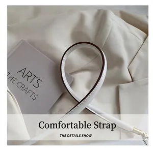 Detail of white leather shoulder strap with brown painted edges and golden metal hardware