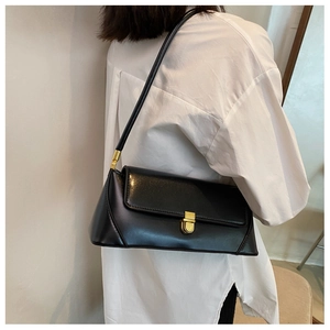 Detail of glossy black baguette bag featuring a gold metal buckle and sleek side profile