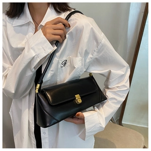 Close-up of black leather baguette bag with gold metal clasp and minimalist strap