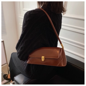 Brown leather baguette bag with gold metal buckle worn over the shoulder by a model