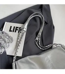 Detail of silver textured leather tote with chain strap on a grey blazer background