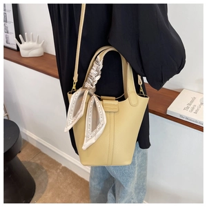 Detail view of beige lychee leather bucket bag with decorative silk scarf on handle
