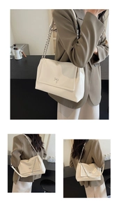Detail of a creamy white glossy tote bag with silver bow accent and chain shoulder strap