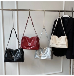Detail of four glossy leather tote bags with metal bows in black, red, silver, and cream
