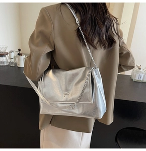 Detail of silver metallic tote bag with bow accent and chain strap worn by a model