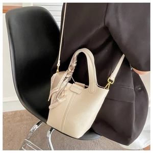 Detail view of cream leather bucket bag with silk scarf on handle and gold hardware detail