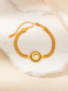 Détail du bracelet doré motif soleil avec double chaîne sur fond de pierre