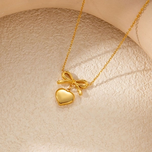 Detailed view of a golden bow and heart pendant necklace on a textured display surface