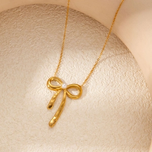 Detailed view of a gold bow necklace pendant with a central pearl in a matte vessel