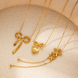 Detailed close-up of golden bow, heart, and flower pendant necklaces with O-chains