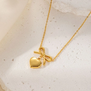 Elegant gold-plated necklace with bow and heart pendants on a textured stone surface