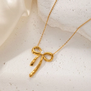 Exquisite golden bow pendant necklace with a white pearl on a textured white stone surface