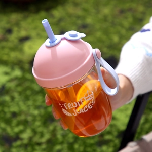 Tragbarer Kunststoff-Saftbecher mit Strohhalm, Griff und frischen Orangenscheiben im Gras