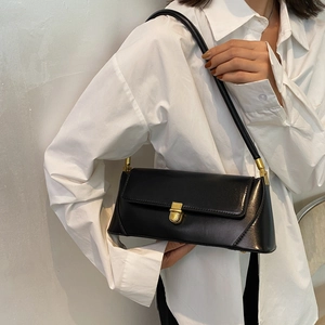 Minimalist black baguette shoulder bag with gold clasp shown on a model in white shirt