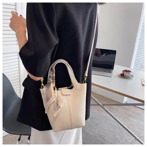 Close-up of cream leather bucket bag with litchi texture and decorative silk scarf