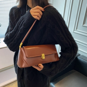 Brown leather baguette shoulder bag featuring gold hardware worn with a black sweater
