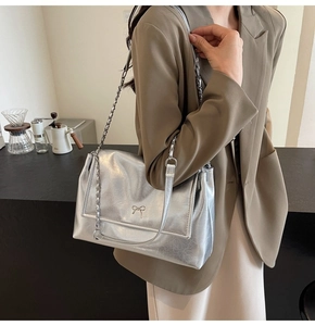 Detail of silver metallic tote with a bow accent and chain strap on a model