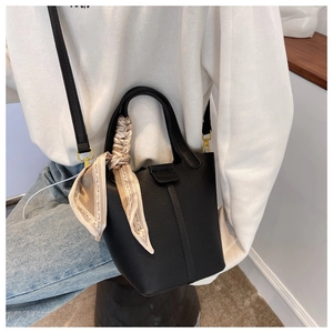 Detail of black pebbled leather bucket bag with decorative silk scarf and gold hardware