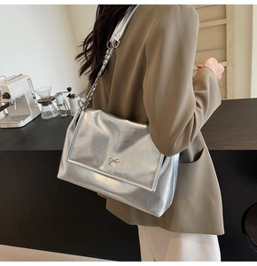 Detailed view of silver shoulder bag with metallic bow clasp and chain strap
