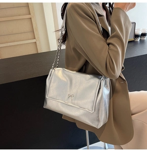 Silver shoulder bag with bow detail and chain strap worn by a model in a minimal setting
