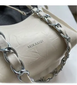 Gros plan sur le cuir froissé crème et la bandoulière chaîne argentée d'un sac à épaule