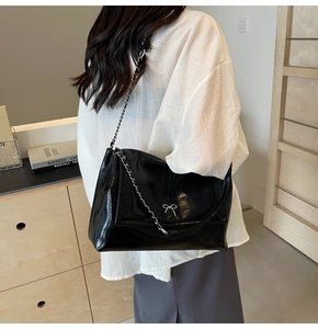 Detail of glossy black shoulder bag featuring silver chain and metal bow accent