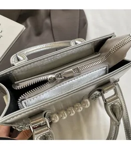 Détail du sac à main argenté métallisé avec fermeture éclair et chaîne en perles