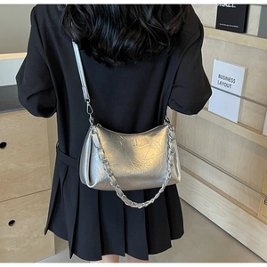 Détail du sac bandoulière argenté plissé avec chaîne en métal sur modèle en robe noire