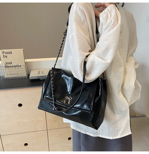 Detail of black glossy tote bag with silver bow hardware and metallic chain strap