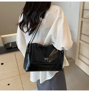 Detail of glossy black tote bag featuring silver bow hardware and leather chain strap