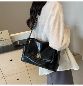 Macro detail of glossy black leather tote featuring silver bow and chain strap