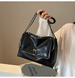 Detail of black soft leather tote bag featuring a silver bow and metal chain strap