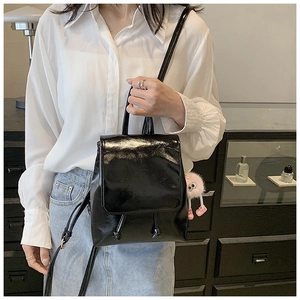 Detail of glossy black mini backpack with pink plush charm on white shirt outfit