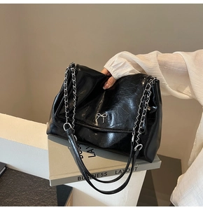 Close-up of black glossy tote bag featuring a silver metal bow buckle and chain strap