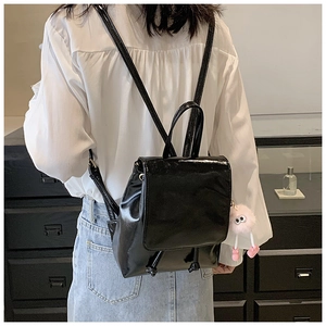 Glossy black patent leather mini backpack with pink plush charm on model back