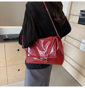 Detail of red glossy leather tote featuring a metallic silver bow and chain strap