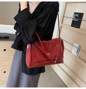 Detail of red patent leather tote with silver bow and chain strap on a model