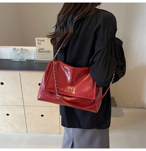 Detail of red glossy shoulder bag with silver bow clasp and metal chain strap detail