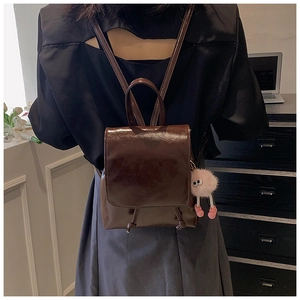 Detail of a shiny dark brown PU leather mini backpack with a pink plush ball accessory