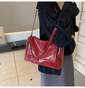 Detail of red wrinkled faux leather tote bag featuring a silver metal bow and chain strap