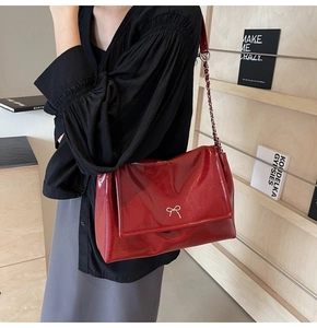 Side view of red glossy patent leather shoulder bag with a silver metal bow accent