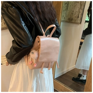 Back view of a pink PU leather mini backpack featuring a plush doll charm on a female model