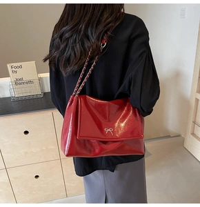Detail of red patent leather tote with silver bow buckle and woven chain strap