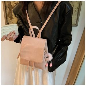Model wearing a mini light pink PU leather backpack with a plush doll charm on the back