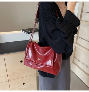 Detail of burgundy glossy leather tote with silver bow logo and metal chain strap
