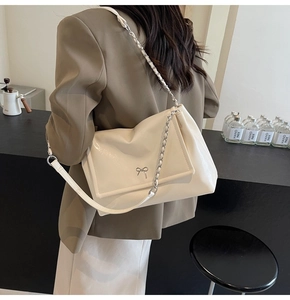 Detail of a beige leather tote with a silver bow clasp on a chain strap