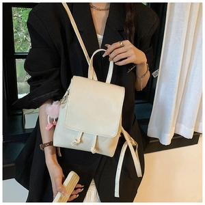 Close-up of creamy white PU backpack with drawstring knots and pink plush charm
