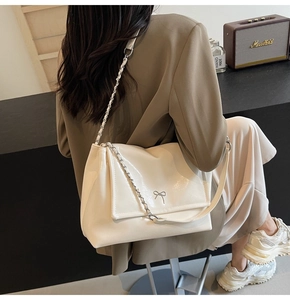Close-up of cream white glossy leather tote with silver bow accent and chain strap detail