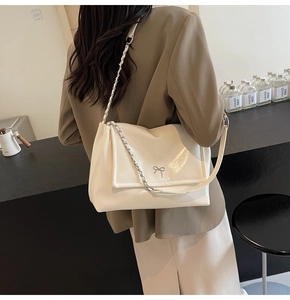 Detail view of cream leather tote bag with silver bow accent on model's shoulder