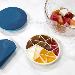 Detail of round silicone ice mold with geometric dividers and blue lid on marble surface